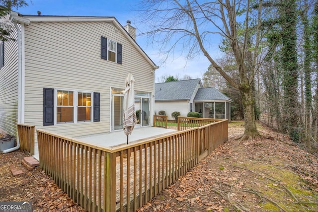 back of property with a deck, a sunroom, and a chimney