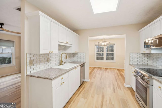 kitchen with stainless steel appliances, sink, white cabinetry, a healthy amount of sunlight, and light stone countertops