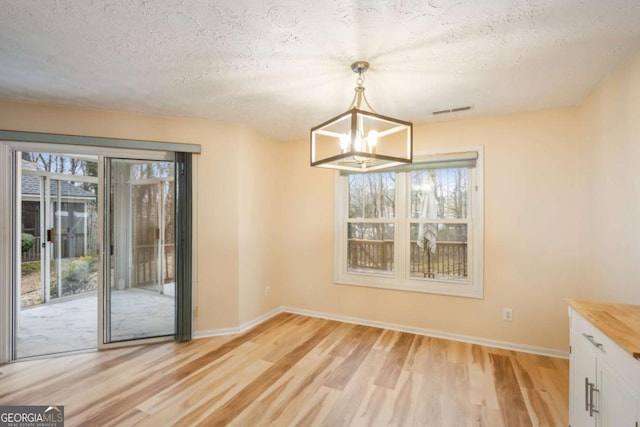 unfurnished dining area with a notable chandelier, light hardwood / wood-style flooring, and a textured ceiling