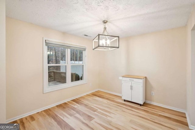 unfurnished dining area featuring an inviting chandelier, a textured ceiling, and light hardwood / wood-style floors