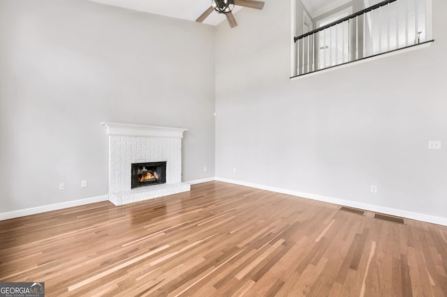 unfurnished living room with ceiling fan, wood-type flooring, a brick fireplace, and a towering ceiling