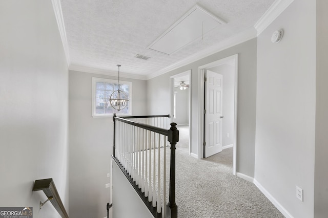 hallway with light colored carpet, ornamental molding, a textured ceiling, and a notable chandelier