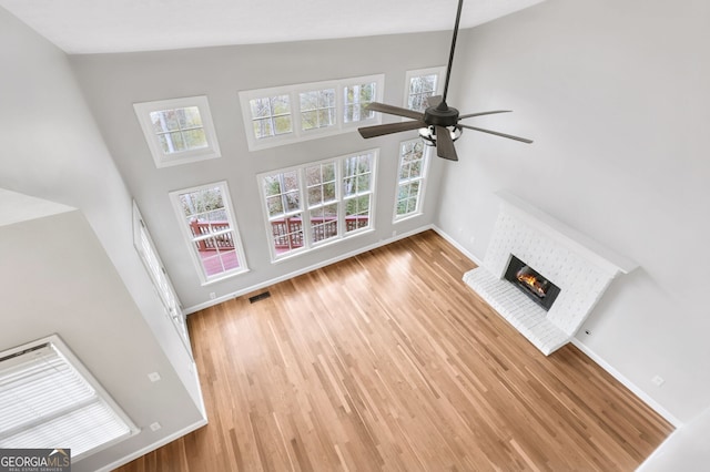 unfurnished living room with high vaulted ceiling, plenty of natural light, a fireplace, and hardwood / wood-style floors