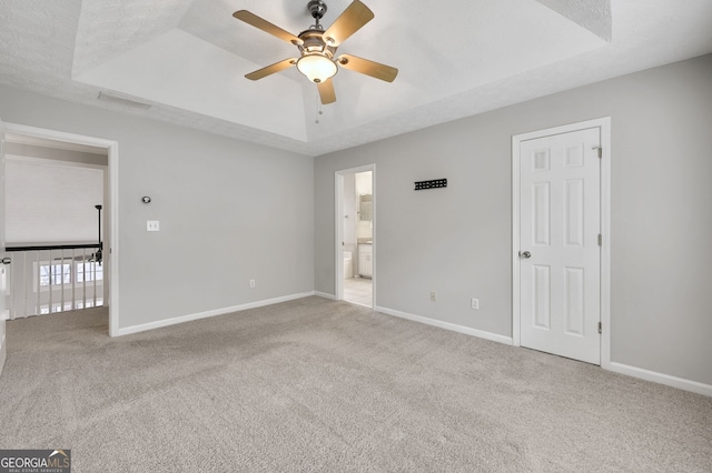 carpeted empty room featuring a textured ceiling, ceiling fan, and a tray ceiling