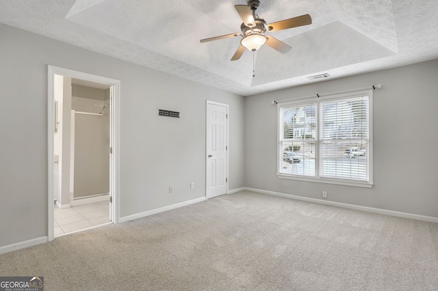 unfurnished bedroom featuring ceiling fan, light colored carpet, a textured ceiling, and a tray ceiling