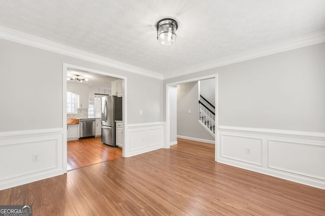 unfurnished living room with crown molding, a textured ceiling, and light wood-type flooring