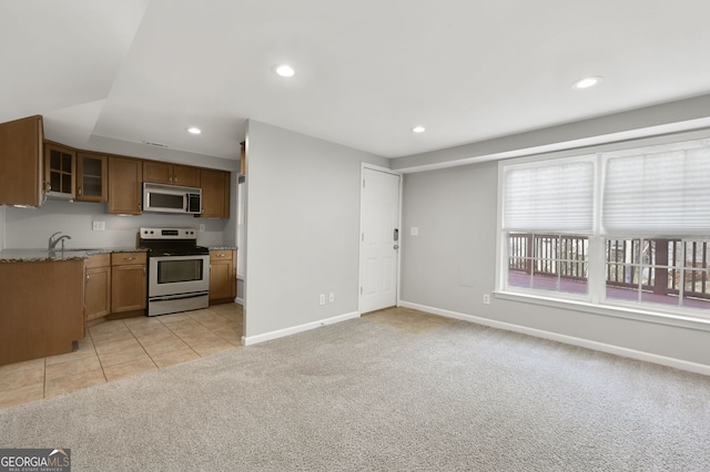 kitchen featuring lofted ceiling, sink, appliances with stainless steel finishes, light stone countertops, and light colored carpet