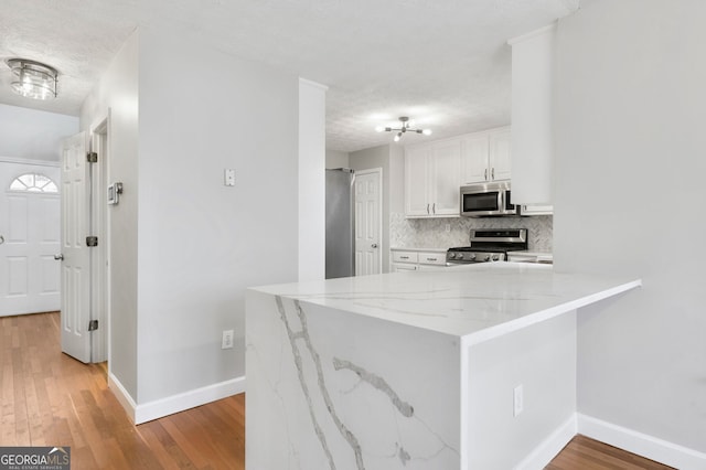 kitchen featuring light hardwood / wood-style flooring, appliances with stainless steel finishes, white cabinetry, decorative backsplash, and kitchen peninsula