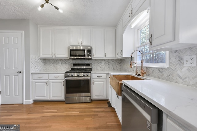 kitchen with stainless steel appliances, sink, light hardwood / wood-style flooring, and white cabinets