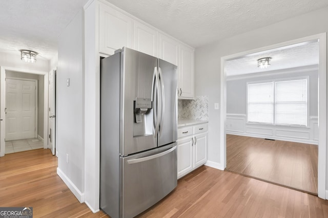 kitchen featuring backsplash, stainless steel refrigerator with ice dispenser, a textured ceiling, white cabinets, and light wood-type flooring