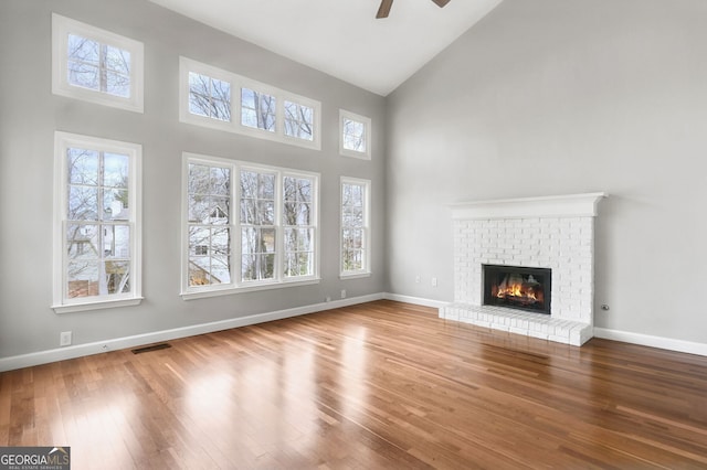 unfurnished living room with a brick fireplace, hardwood / wood-style flooring, high vaulted ceiling, and ceiling fan