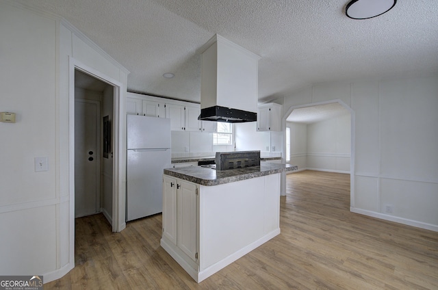 kitchen featuring a textured ceiling, light wood-type flooring, white refrigerator, a kitchen island, and white cabinets