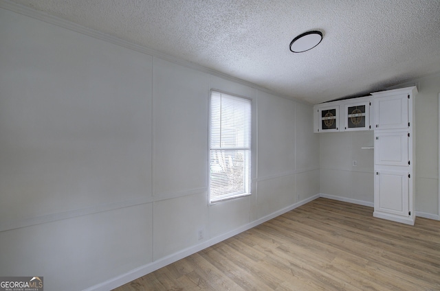 spare room with lofted ceiling, a textured ceiling, and light hardwood / wood-style floors