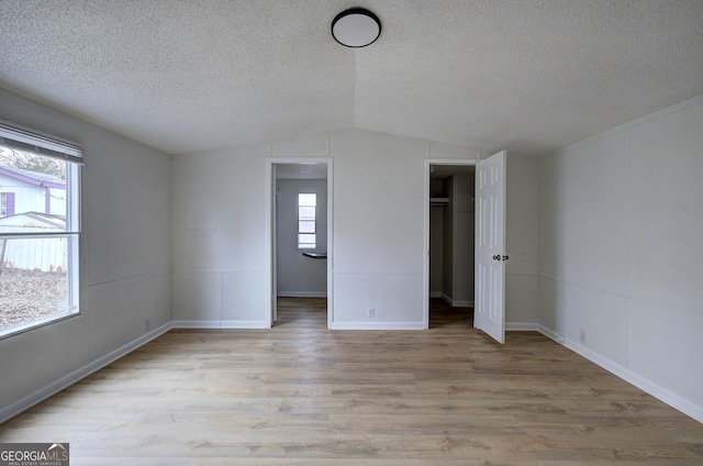 unfurnished bedroom with vaulted ceiling, a textured ceiling, and light hardwood / wood-style flooring