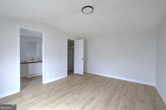 unfurnished bedroom with vaulted ceiling, sink, a textured ceiling, and light hardwood / wood-style flooring