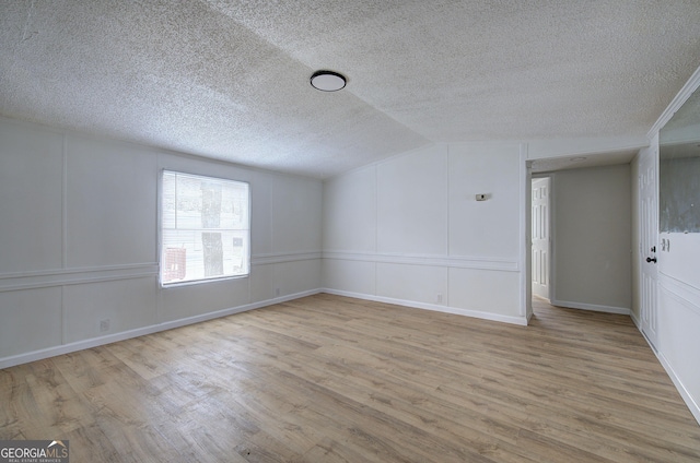 spare room with light hardwood / wood-style flooring, a textured ceiling, and vaulted ceiling