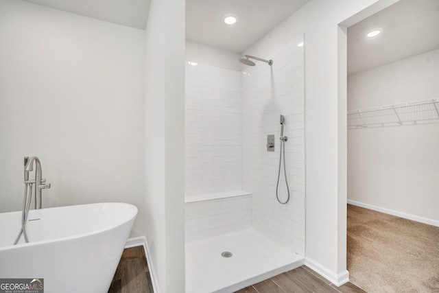 full bath featuring baseboards, wood finished floors, a tile shower, a walk in closet, and a freestanding tub