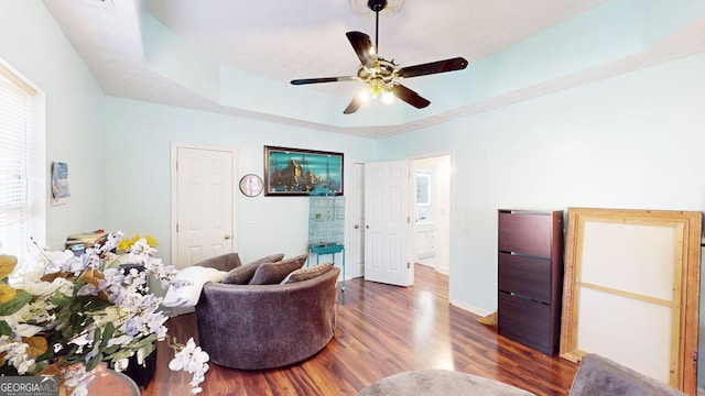 living room featuring dark wood-type flooring, ceiling fan, and a raised ceiling