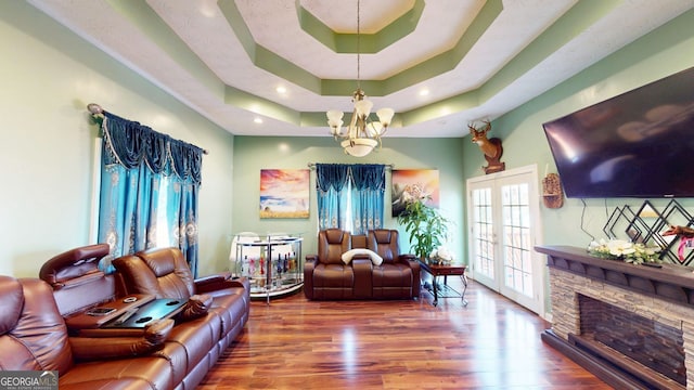 living room with french doors, wood-type flooring, a tray ceiling, and a stone fireplace