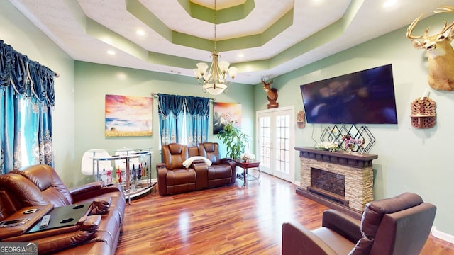 living room featuring french doors, wood-type flooring, a chandelier, a tray ceiling, and a fireplace