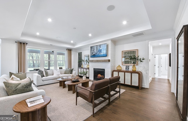 living room with a fireplace, ornamental molding, dark hardwood / wood-style floors, and a raised ceiling