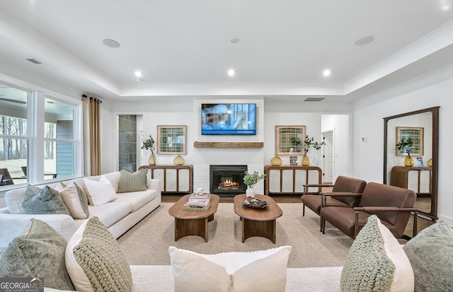 living room featuring a brick fireplace, crown molding, light hardwood / wood-style flooring, and a raised ceiling