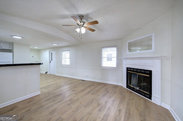 unfurnished living room featuring vaulted ceiling, ceiling fan, light hardwood / wood-style floors, and a textured ceiling