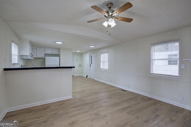 kitchen featuring vaulted ceiling, light hardwood / wood-style flooring, fridge, kitchen peninsula, and white cabinets