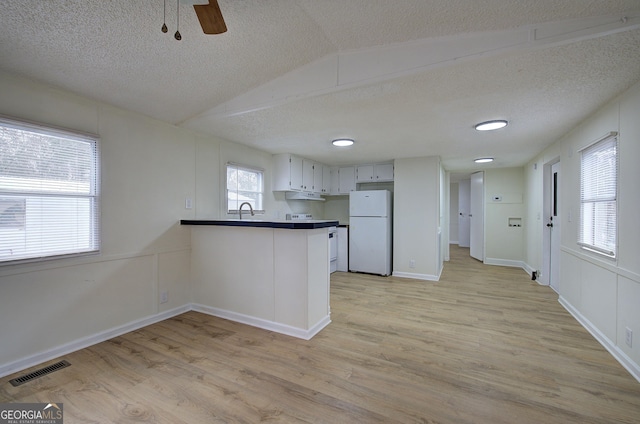 kitchen featuring light hardwood / wood-style floors, kitchen peninsula, vaulted ceiling, and white fridge