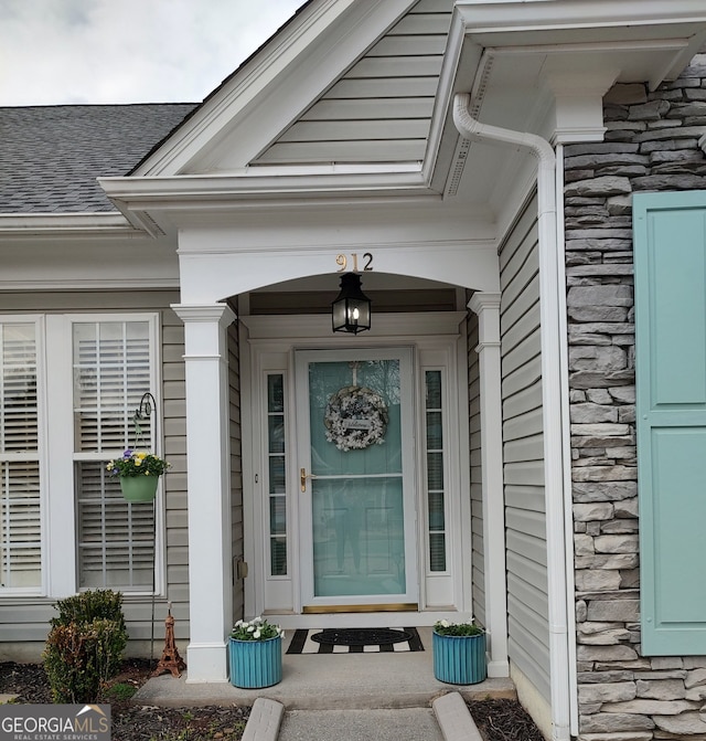 property entrance with stone siding, a porch, and a shingled roof