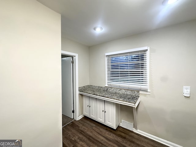 kitchen featuring white cabinetry, built in desk, light stone counters, and dark hardwood / wood-style flooring