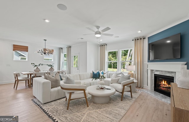 living room with crown molding, a high end fireplace, ceiling fan with notable chandelier, and light hardwood / wood-style floors