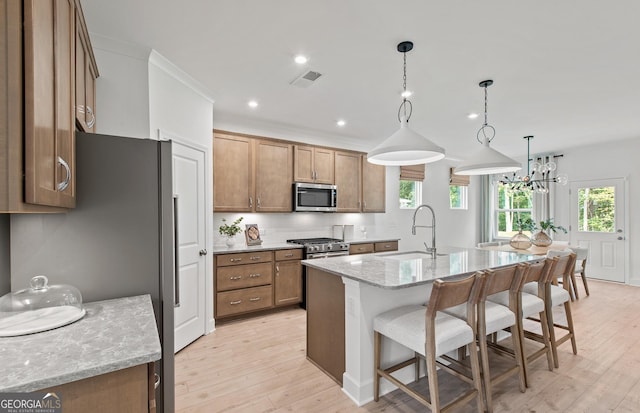 kitchen with pendant lighting, sink, stainless steel appliances, light stone countertops, and a center island with sink