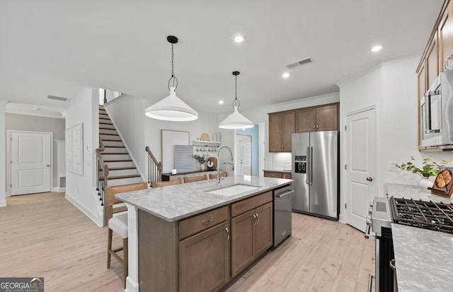 kitchen with sink, appliances with stainless steel finishes, light stone countertops, an island with sink, and decorative light fixtures