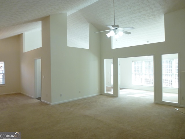 unfurnished living room with baseboards, high vaulted ceiling, a healthy amount of sunlight, and light colored carpet