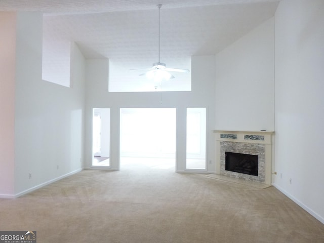 unfurnished living room featuring light carpet, a towering ceiling, a fireplace, and a ceiling fan