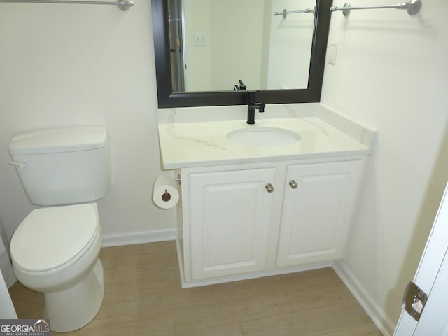 half bath featuring baseboards, vanity, and toilet