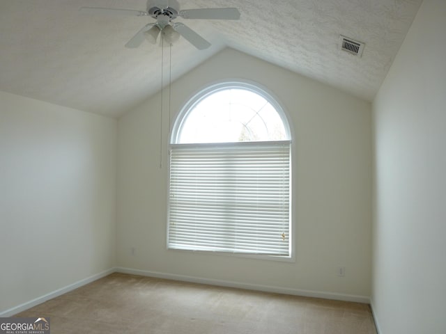 spare room featuring visible vents, vaulted ceiling, a textured ceiling, and light colored carpet