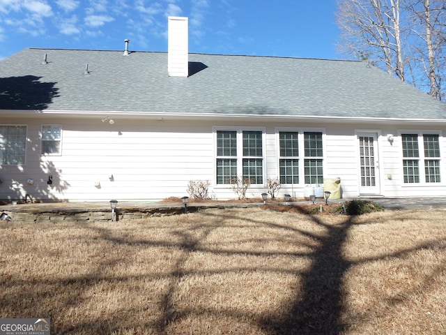 back of property featuring roof with shingles, a chimney, and a yard