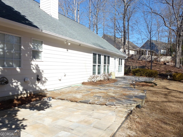 rear view of house featuring a shingled roof, a patio area, and a chimney