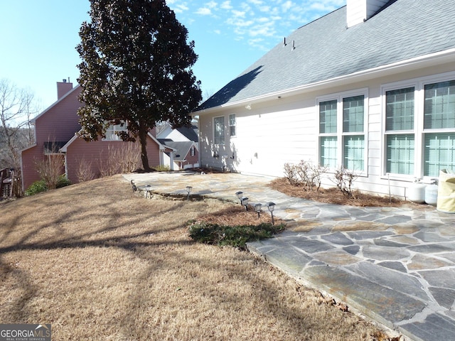 view of home's exterior with roof with shingles, a chimney, and a patio