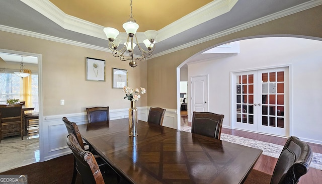 dining space featuring an inviting chandelier, crown molding, a raised ceiling, and french doors