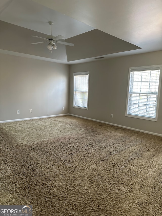 carpeted spare room featuring a raised ceiling and ceiling fan