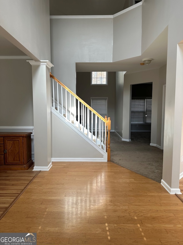 stairway with hardwood / wood-style floors, crown molding, decorative columns, and a high ceiling