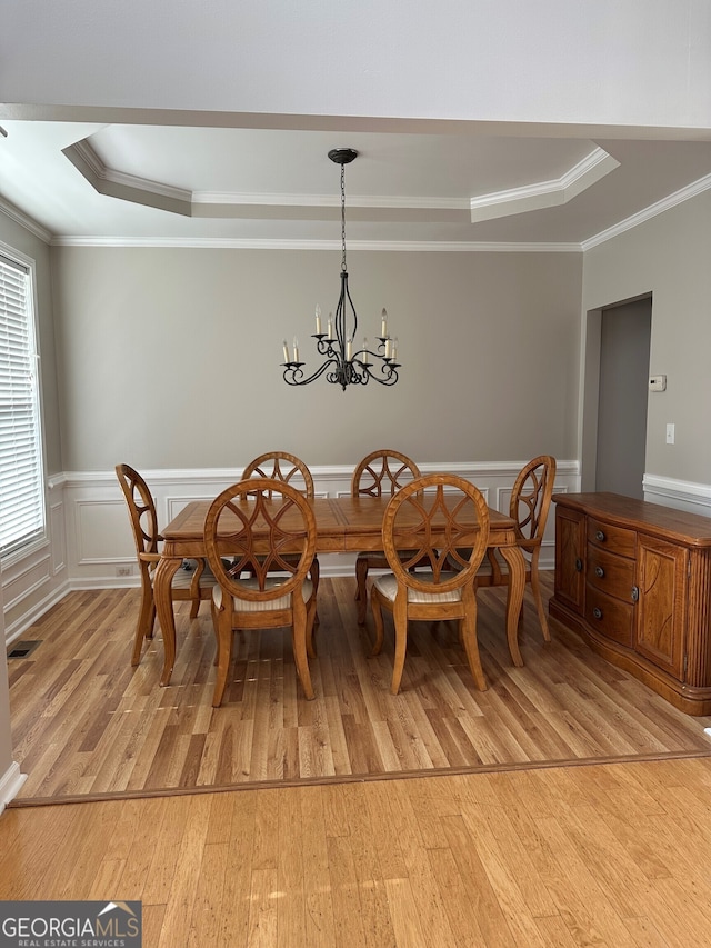 dining space with crown molding, a tray ceiling, a chandelier, and light hardwood / wood-style flooring