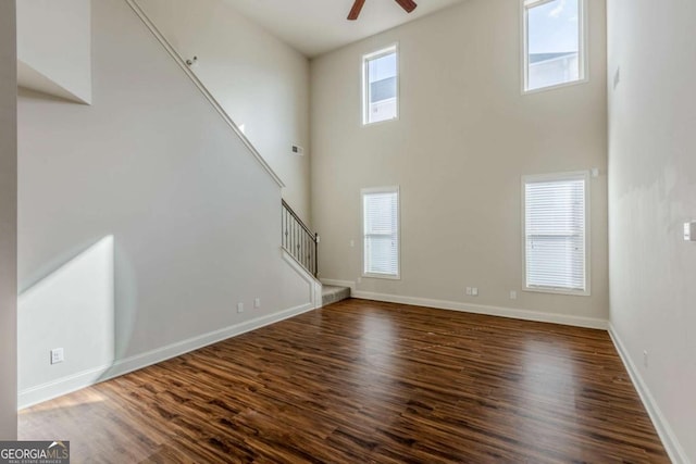 unfurnished living room featuring ceiling fan, dark hardwood / wood-style floors, and a high ceiling