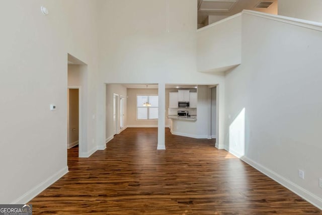 unfurnished living room featuring a high ceiling and dark wood-type flooring