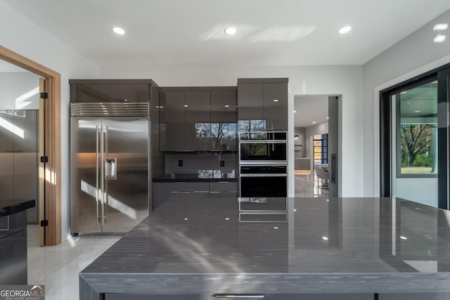 kitchen featuring dark stone countertops, tasteful backsplash, and built in refrigerator