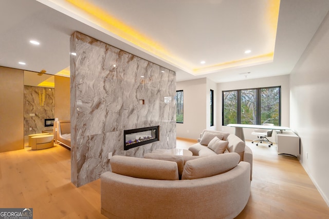 living room with a tray ceiling, light wood-type flooring, and a multi sided fireplace