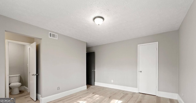 unfurnished bedroom featuring connected bathroom, a textured ceiling, and light hardwood / wood-style floors